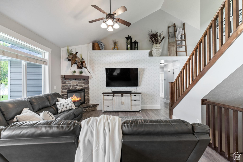 Living room with wood finished floors, lofted ceiling, a ceiling fan, a stone fireplace, and stairway