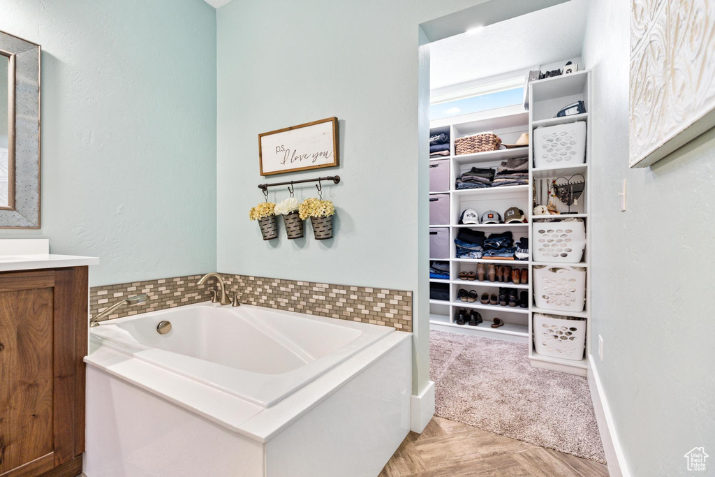 Full bath featuring vanity, a garden tub, a spacious closet, and baseboards