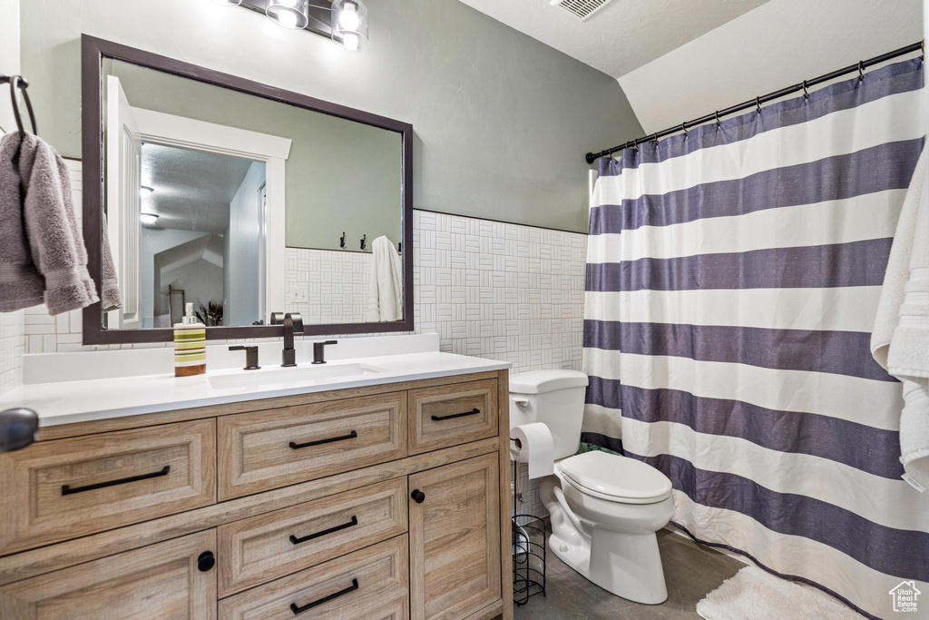 Bathroom with tile walls, toilet, vanity, backsplash, and vaulted ceiling