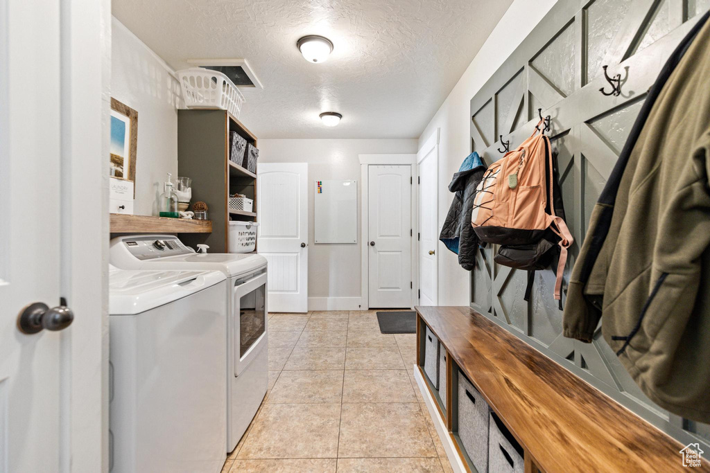 Washroom with independent washer and dryer, a textured ceiling, and light tile patterned floors