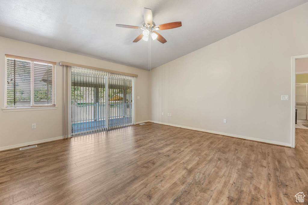 Unfurnished room featuring a ceiling fan, wood finished floors, plenty of natural light, baseboards, and vaulted ceiling