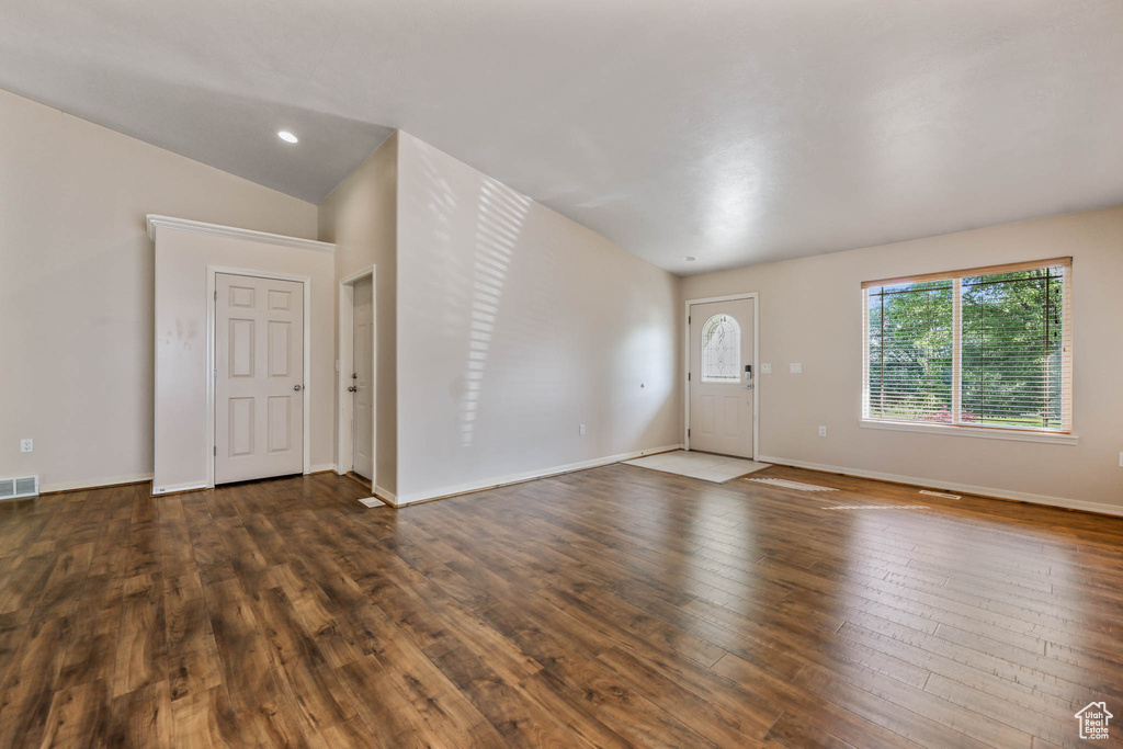 Unfurnished living room with dark wood-style floors, baseboards, and lofted ceiling