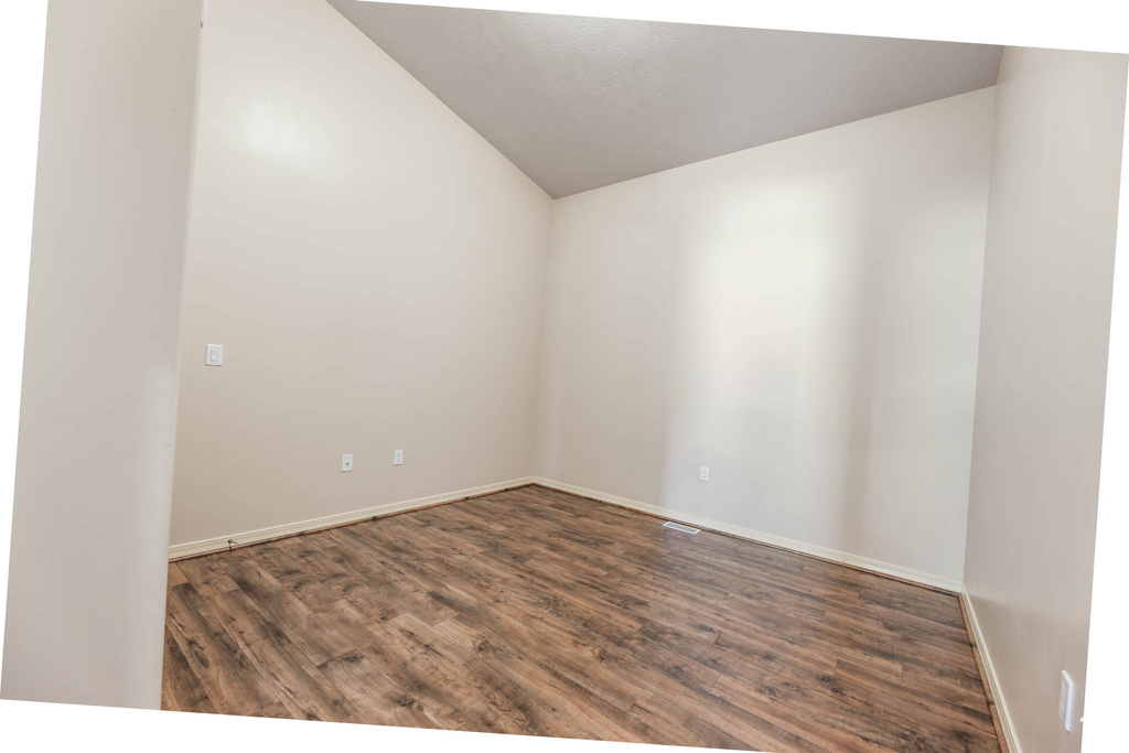 Spare room featuring vaulted ceiling, wood finished floors, and baseboards