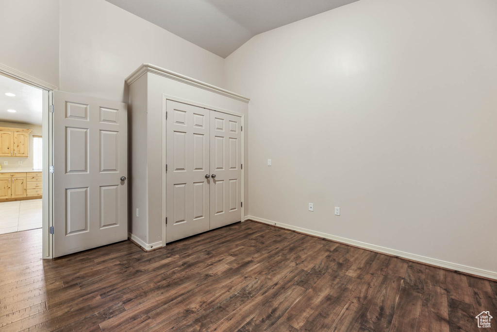 Unfurnished bedroom with lofted ceiling, dark wood finished floors, baseboards, and a closet