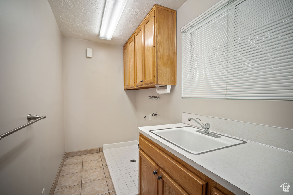 Laundry room featuring cabinet space, washer hookup, baseboards, a textured ceiling, and light tile patterned flooring