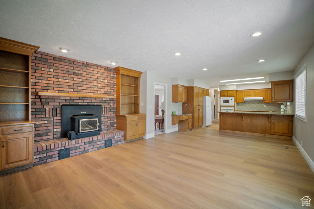 Unfurnished living room featuring light wood-style flooring, baseboards, a wood stove, recessed lighting, and a textured ceiling