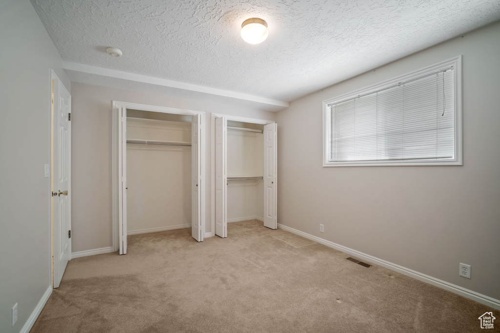 Unfurnished bedroom with two closets, a textured ceiling, carpet, and baseboards