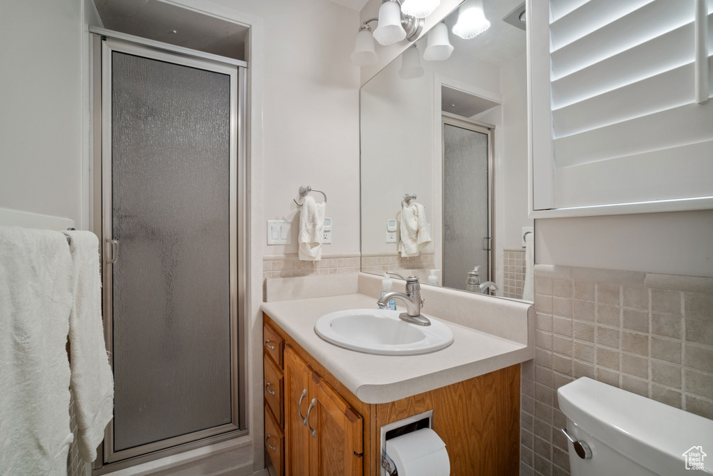 Full bathroom featuring vanity, a shower stall, tile walls, toilet, and wainscoting