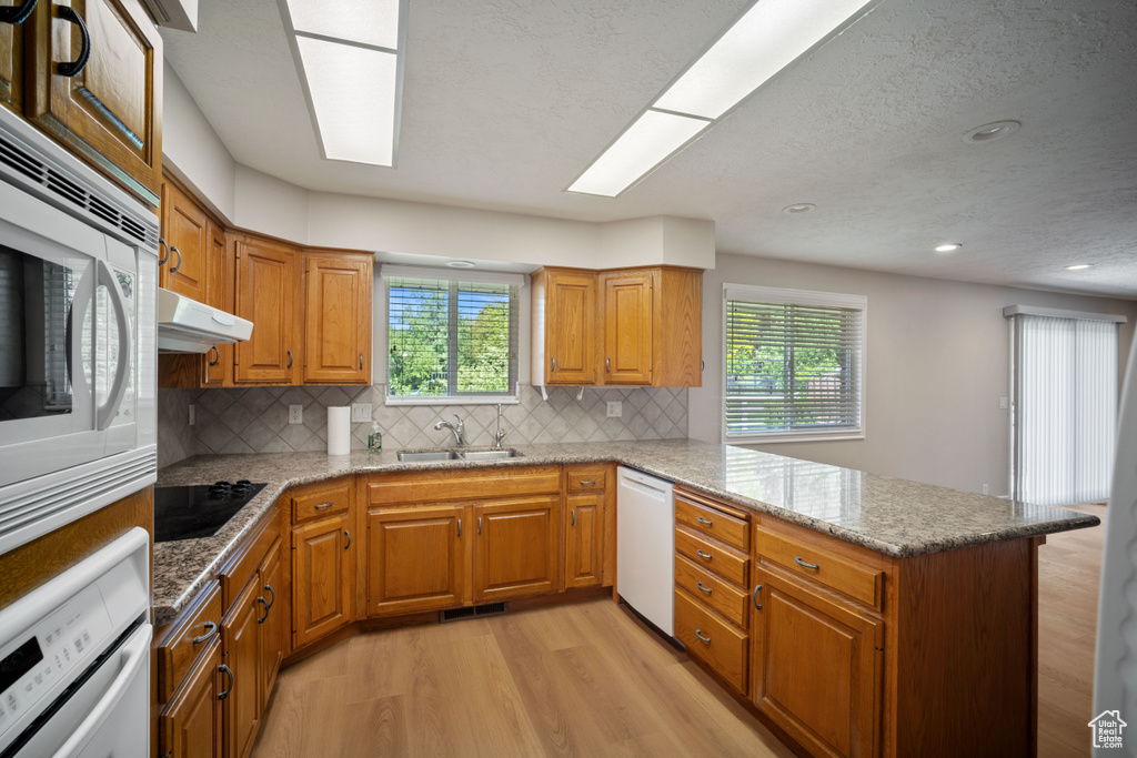 Kitchen featuring white appliances, a peninsula, light wood-style floors, healthy amount of natural light, and recessed lighting