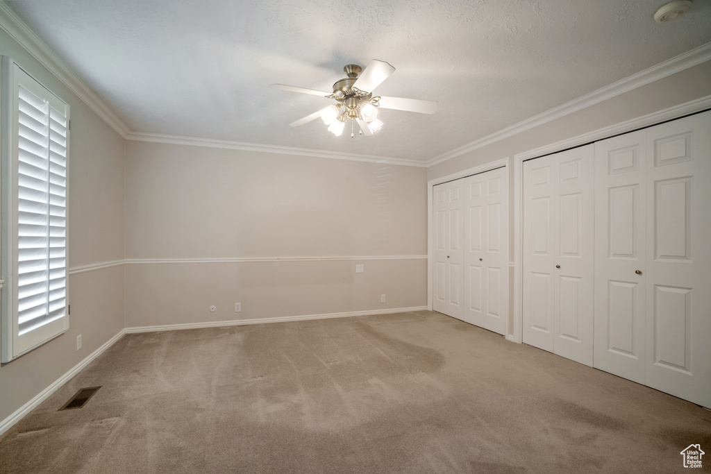 Unfurnished bedroom featuring multiple closets, light carpet, baseboards, crown molding, and multiple windows