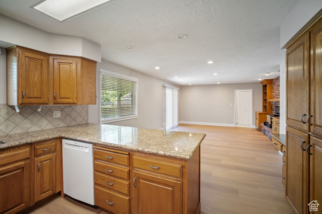Kitchen with white dishwasher, a peninsula, light wood-style flooring, backsplash, and brown cabinets