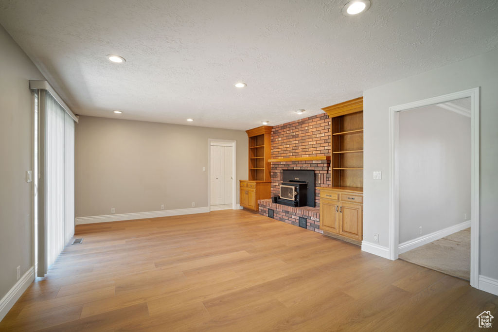 Unfurnished living room with a textured ceiling, baseboards, recessed lighting, light wood-type flooring, and a wood stove