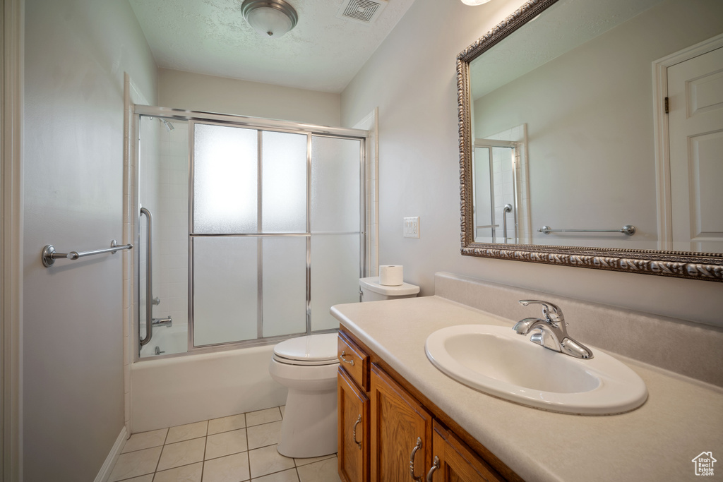 Full bath featuring vanity, toilet, tile patterned flooring, bath / shower combo with glass door, and a textured ceiling