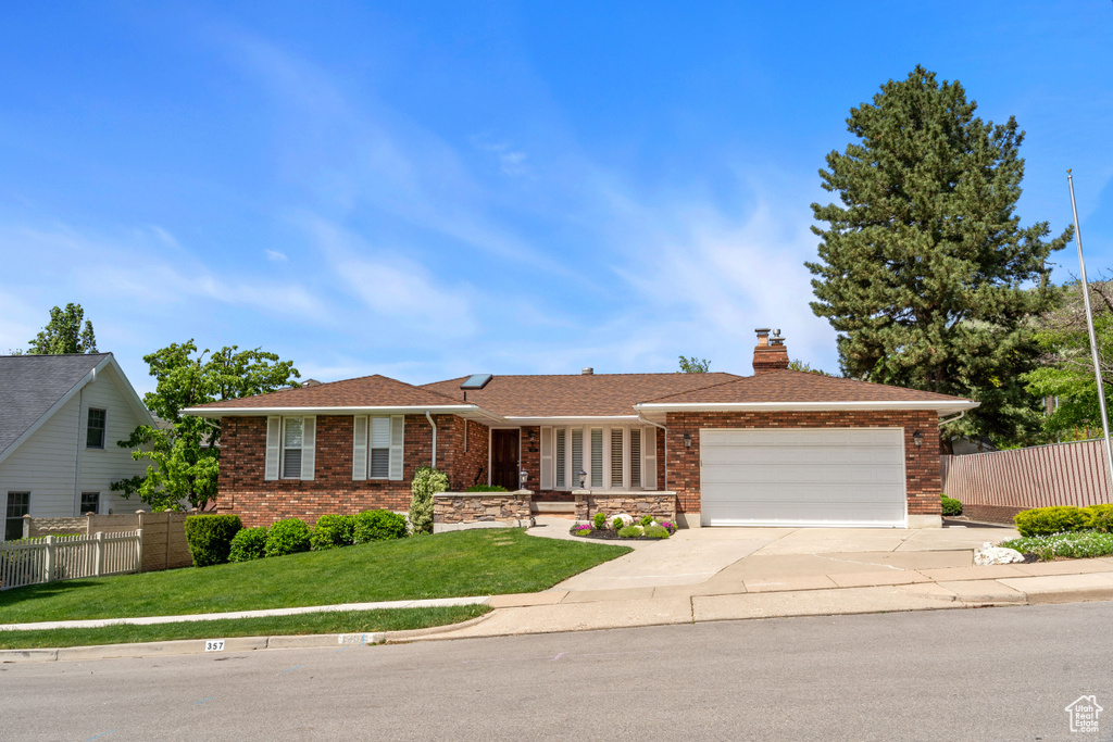 Ranch-style house with an attached garage, driveway, a chimney, and brick siding