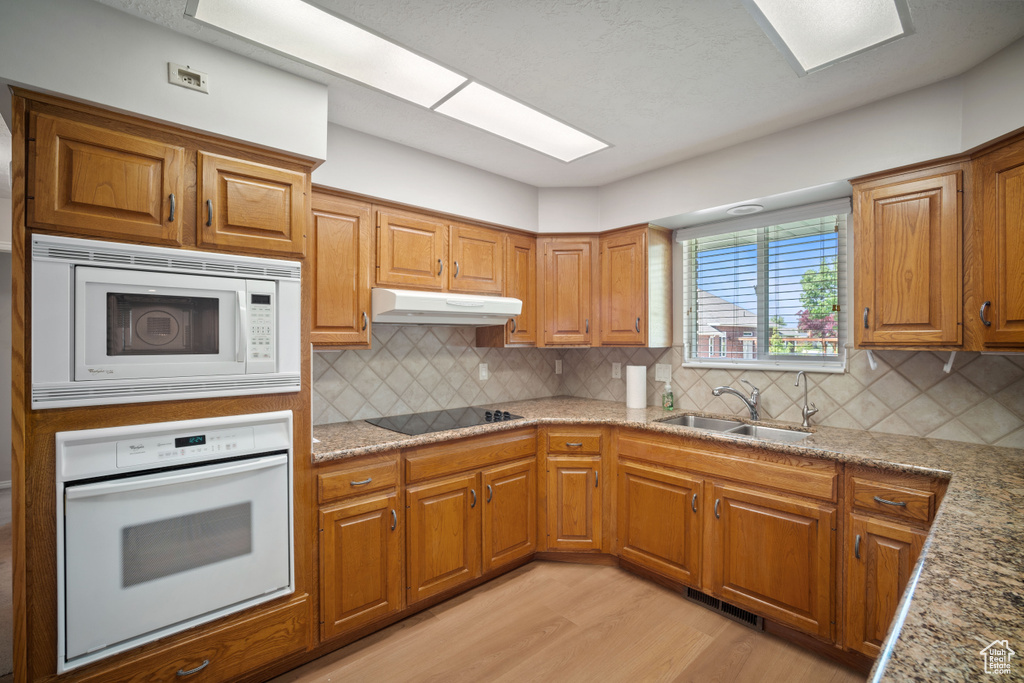 Kitchen with white appliances, a sink, under cabinet range hood, light wood-style floors, and brown cabinets