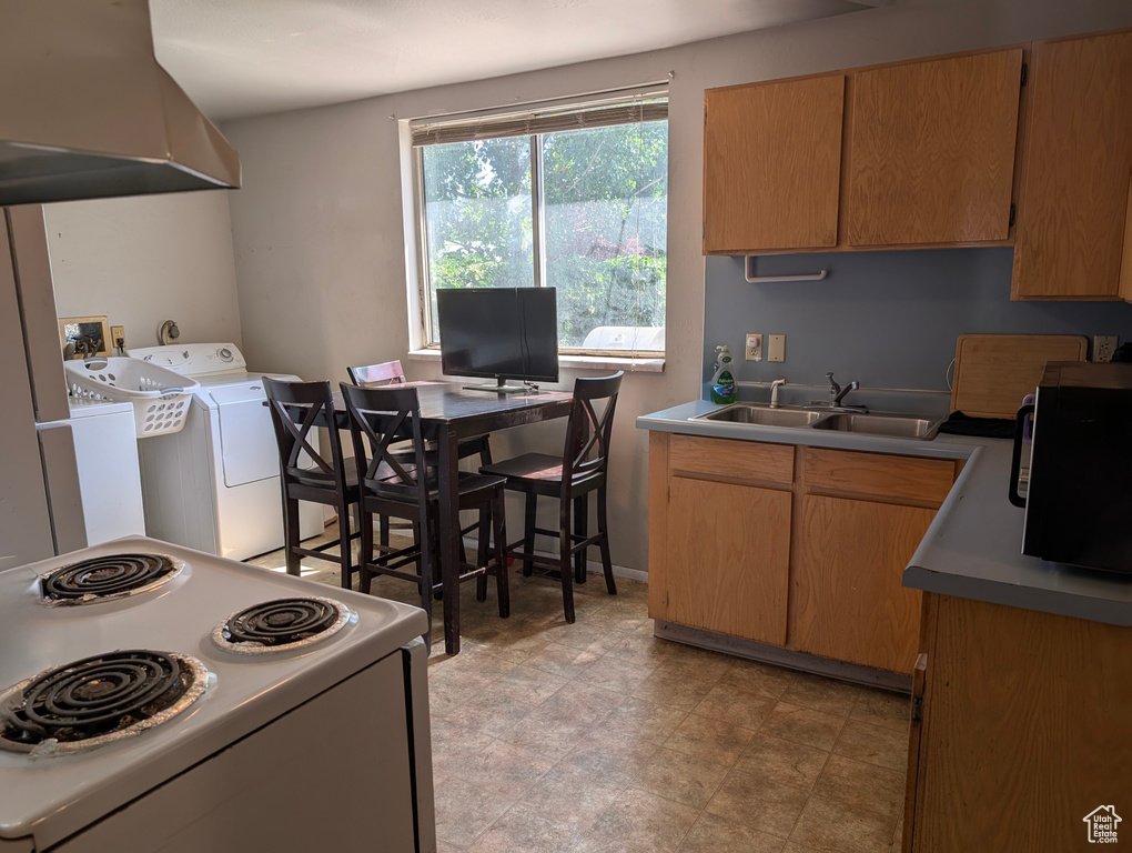 Kitchen with white electric range oven, independent washer and dryer, and a sink