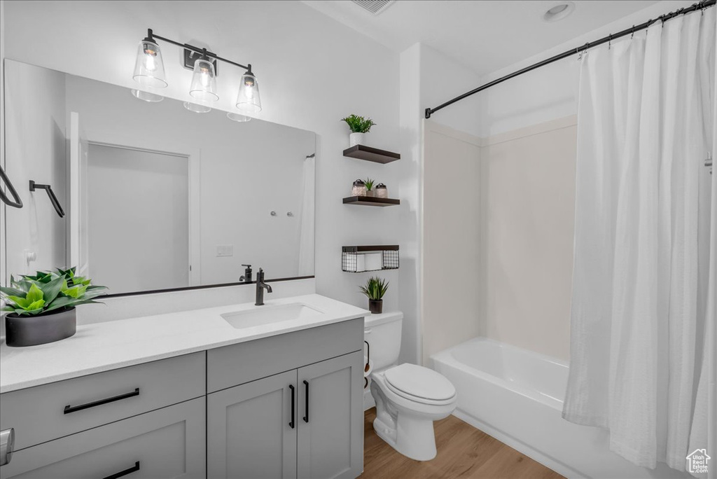 Full bathroom with wood finished floors, vanity, toilet, and shower / bathtub combination with curtain
