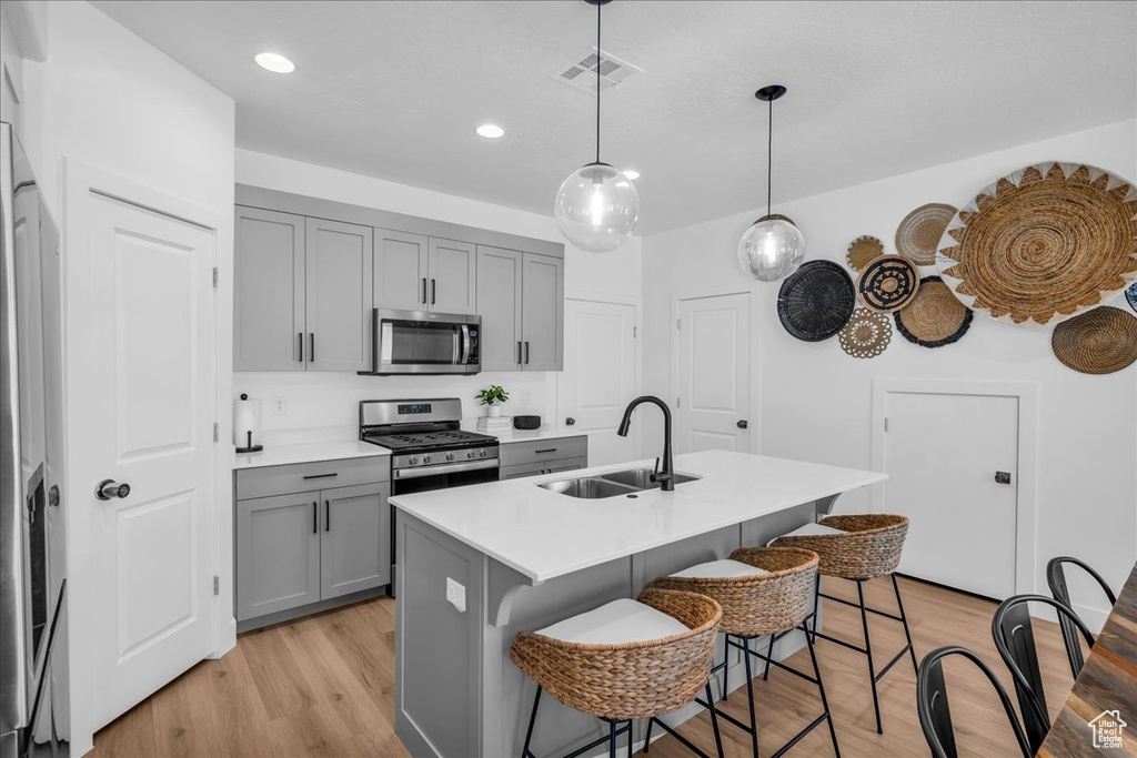Kitchen with stainless steel appliances, a sink, gray cabinetry, a breakfast bar, and light wood-type flooring
