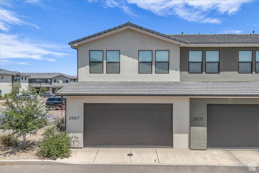 View of front of property featuring a garage, a tile roof, and stucco siding