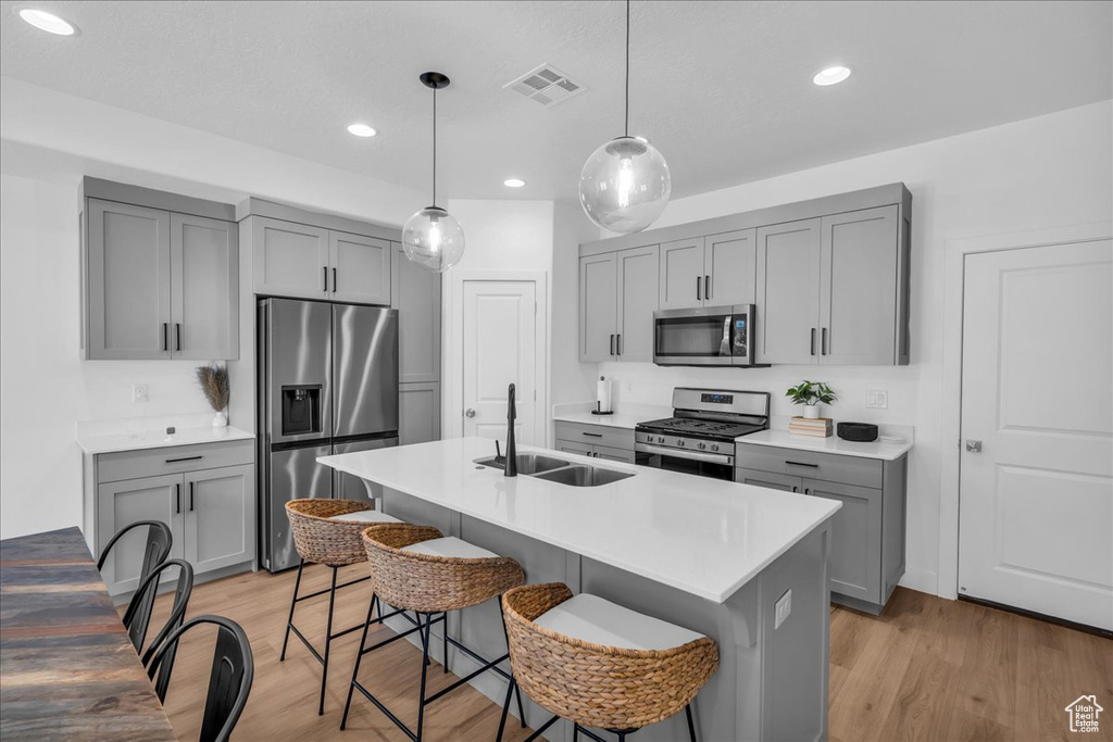 Kitchen featuring appliances with stainless steel finishes, gray cabinetry, a sink, a breakfast bar, and recessed lighting