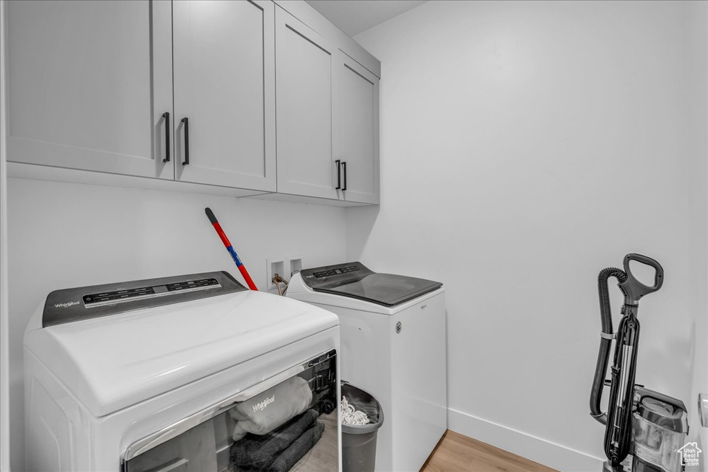 Laundry room with cabinet space, washing machine and clothes dryer, light wood finished floors, and baseboards