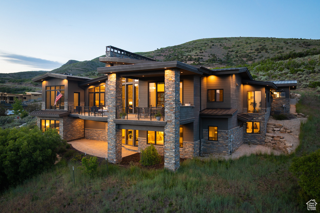 Rear view of house with stone siding, a balcony, a standing seam roof, a mountain view, and metal roof