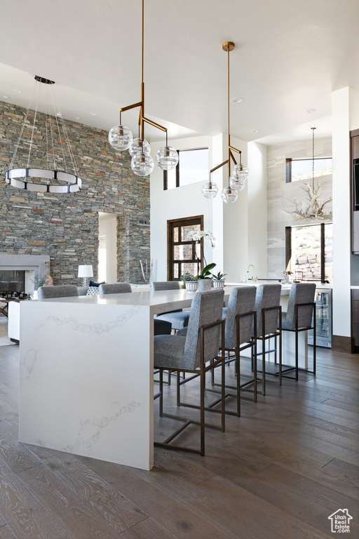 Kitchen with dark wood-style floors, a chandelier, wine cooler, a towering ceiling, and a kitchen bar