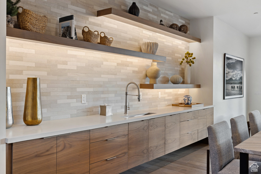 Bar featuring tasteful backsplash, a sink, and dark wood-style floors