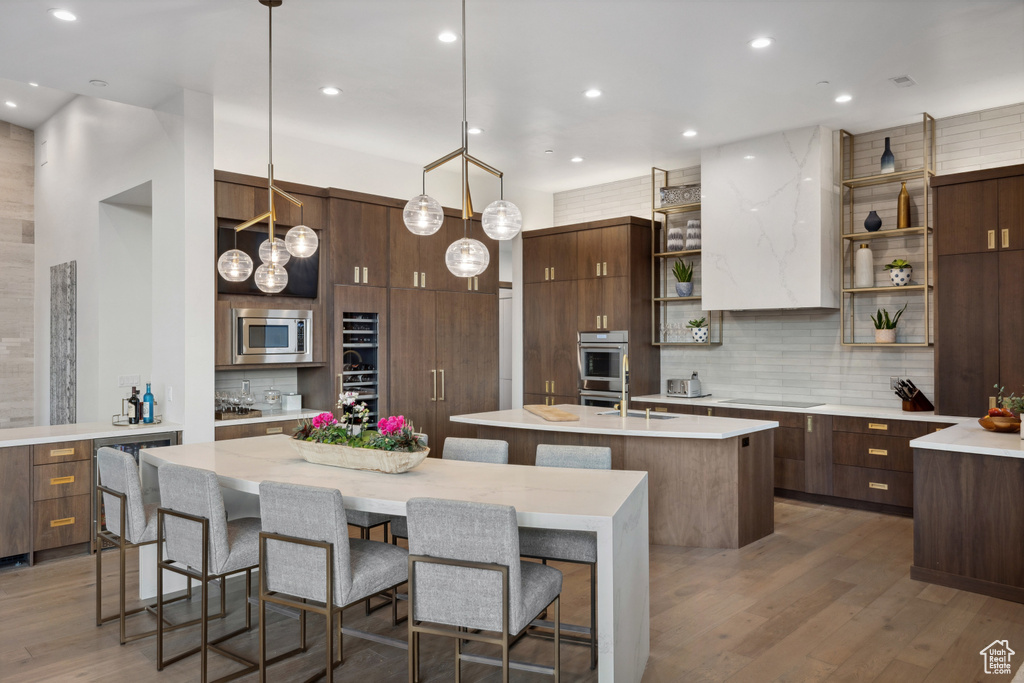 Kitchen with open shelves, an island with sink, decorative backsplash, stainless steel appliances, and wood finished floors