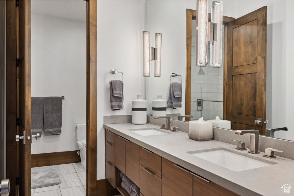 Bathroom featuring toilet, double vanity, marble look tile flooring, a shower with door, and baseboards