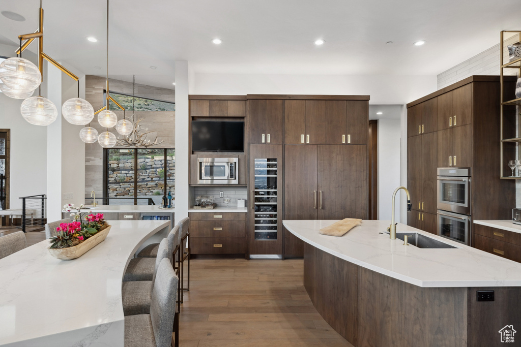 Kitchen with stainless steel appliances, a sink, light wood-type flooring, an island with sink, and recessed lighting