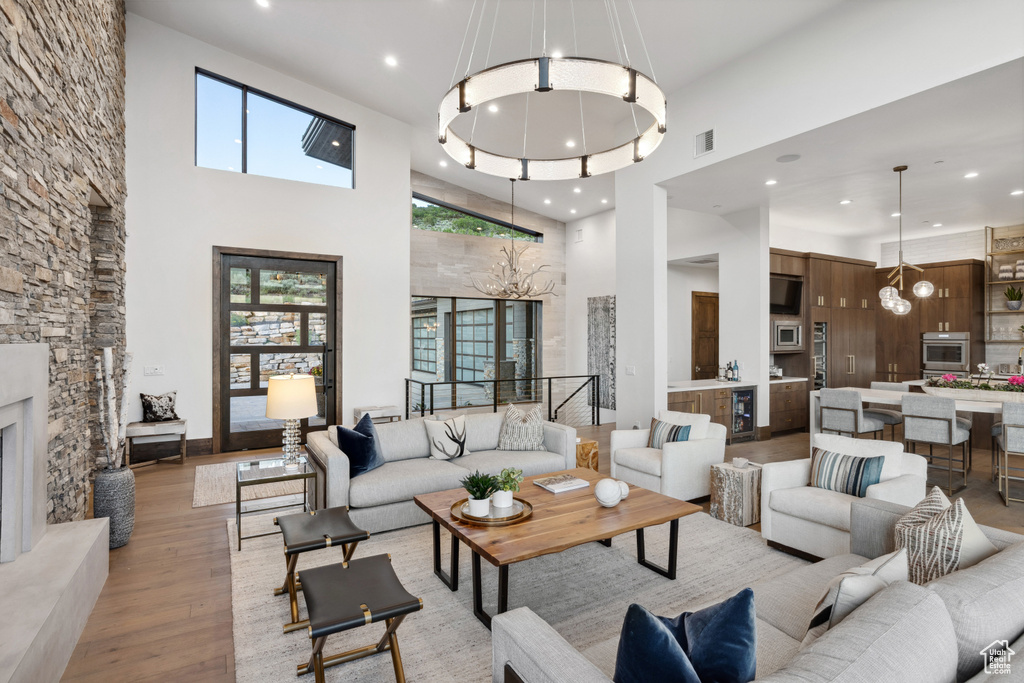 Living area featuring a chandelier, light wood-type flooring, a high ceiling, recessed lighting, and beverage cooler