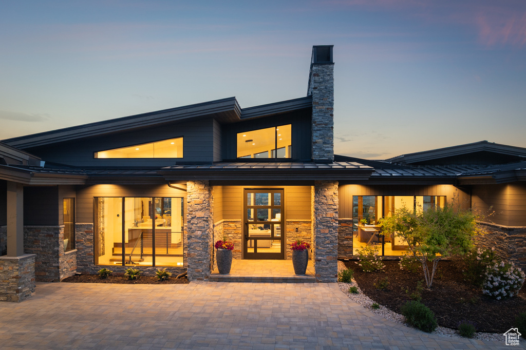 View of front of property with a standing seam roof, stone siding, metal roof, a chimney, and a porch