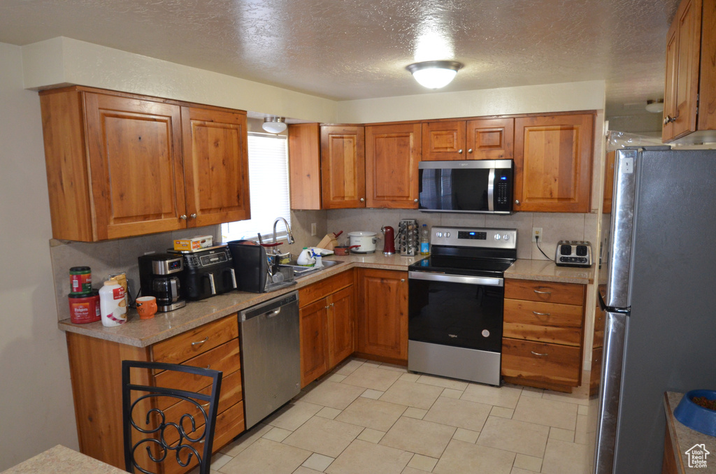 Kitchen featuring stainless steel appliances, brown cabinets, and a textured ceiling