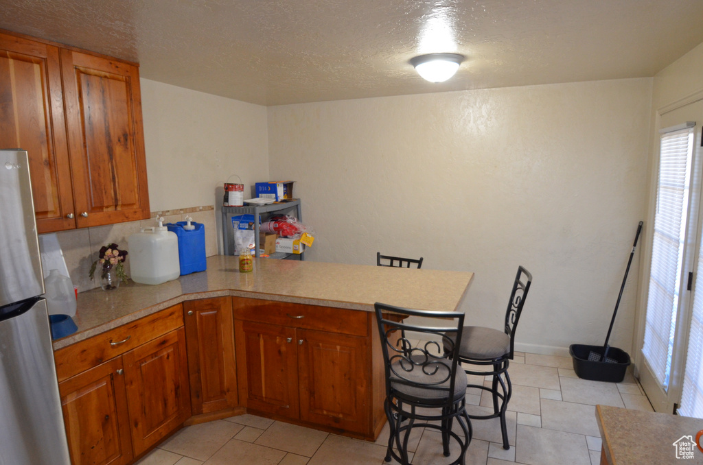 Kitchen featuring freestanding refrigerator, a peninsula, light countertops, brown cabinets, and a textured ceiling
