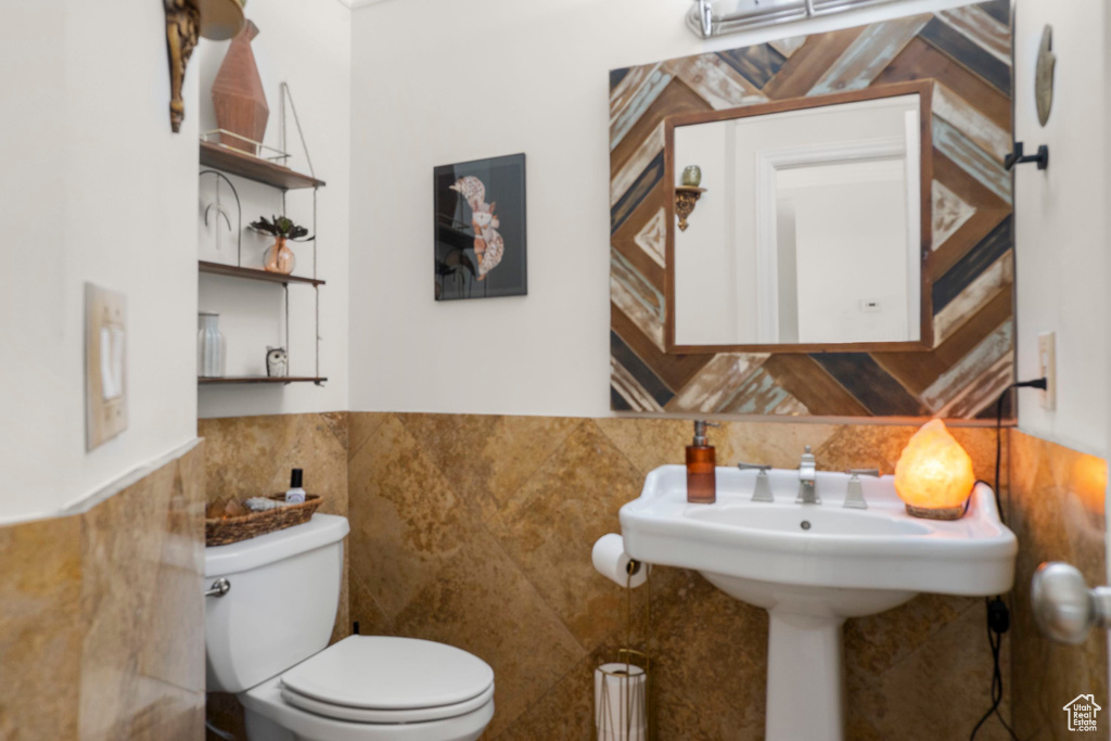 Half bath featuring tile walls, toilet, and wainscoting