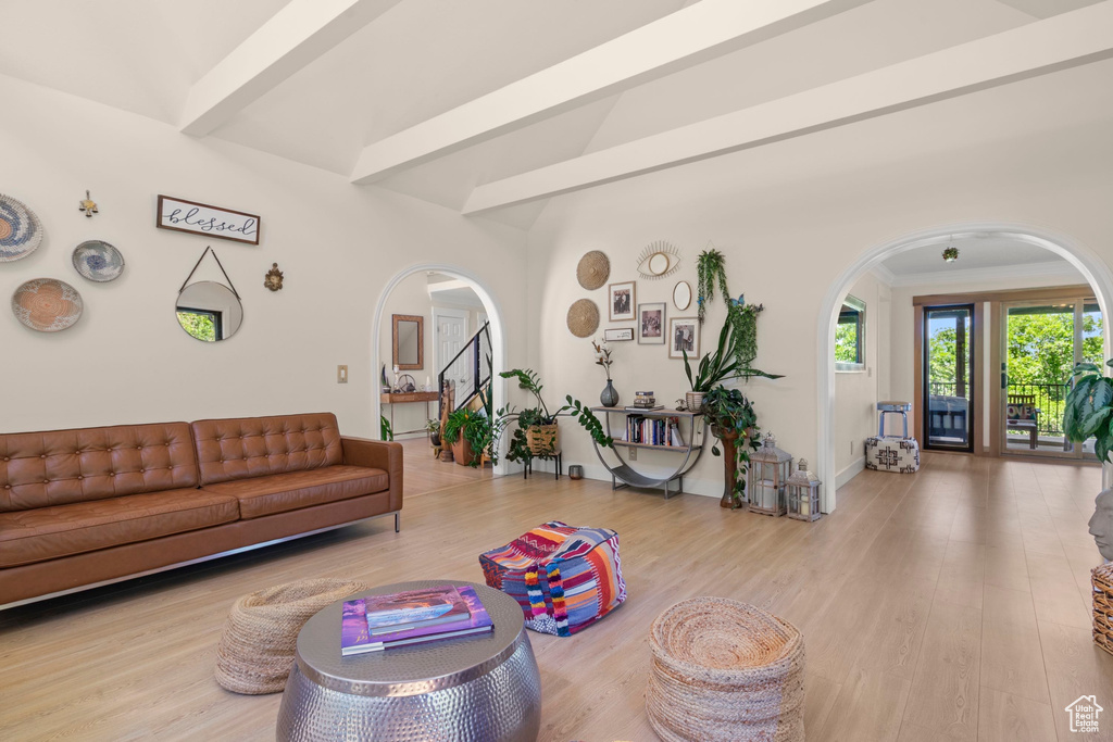 Living area with arched walkways, wood finished floors, baseboards, and beam ceiling