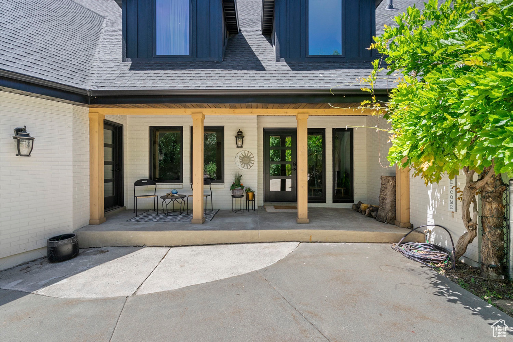 Entrance to property with brick siding, roof with shingles, and a porch