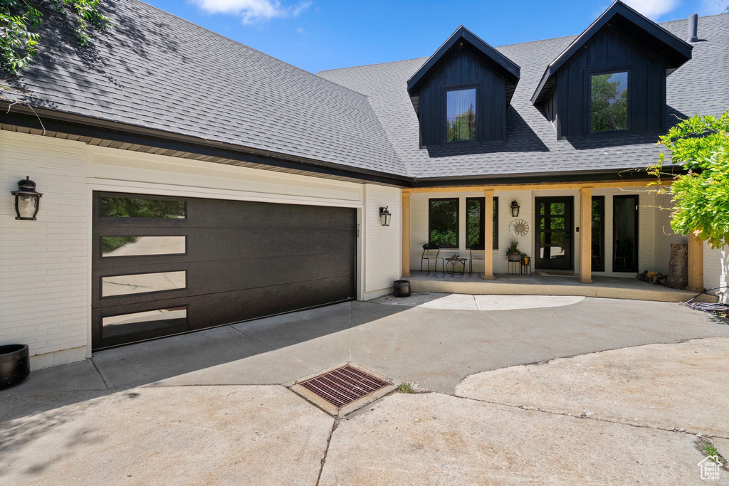 Modern farmhouse featuring driveway, roof with shingles, brick siding, and an attached garage