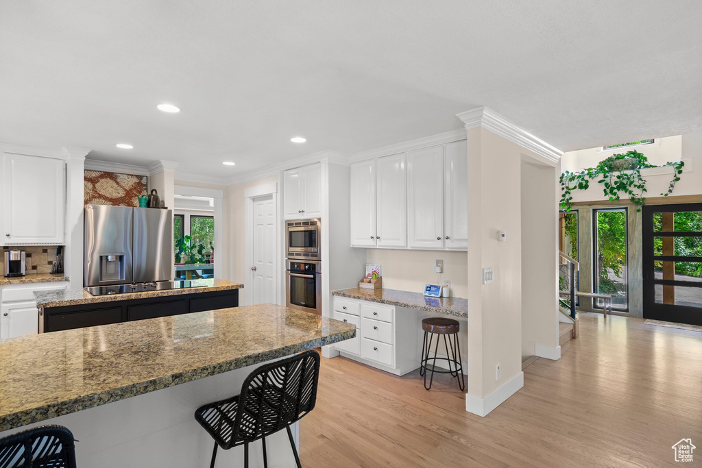 Kitchen with stainless steel appliances, a breakfast bar area, light wood-style floors, plenty of natural light, and recessed lighting