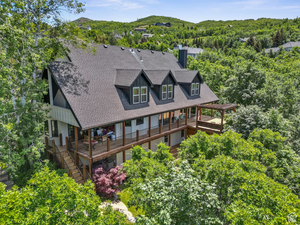 Rear view of property featuring roof with shingles, a chimney, a wooden deck, and a forest view