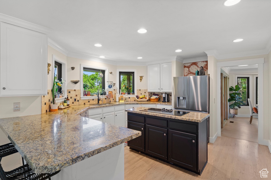 Kitchen with electric cooktop, stainless steel fridge, a sink, white cabinetry, and recessed lighting