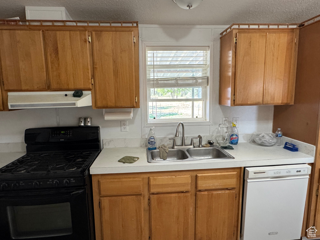 Kitchen with white dishwasher, black gas range, under cabinet range hood, a sink, and light countertops