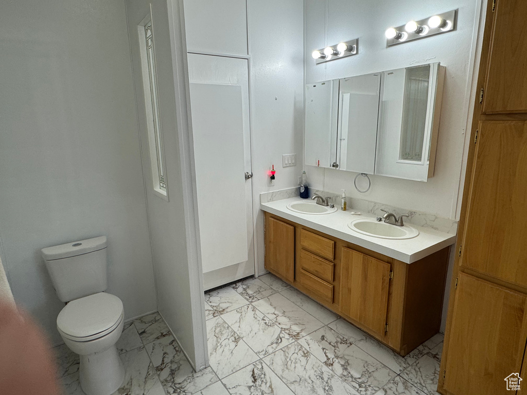 Bathroom featuring marble look tiles, double vanity, and toilet