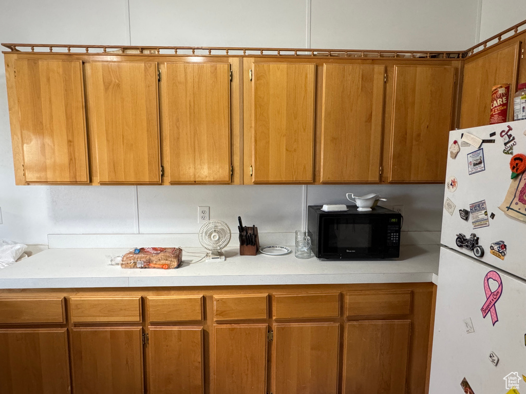 Kitchen featuring freestanding refrigerator, black microwave, light countertops, and brown cabinets