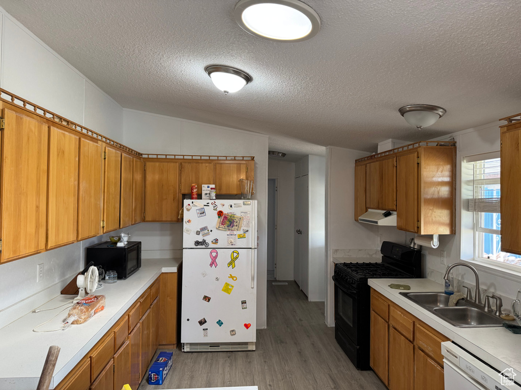 Kitchen with black appliances, a sink, a textured ceiling, brown cabinetry, and light wood finished floors