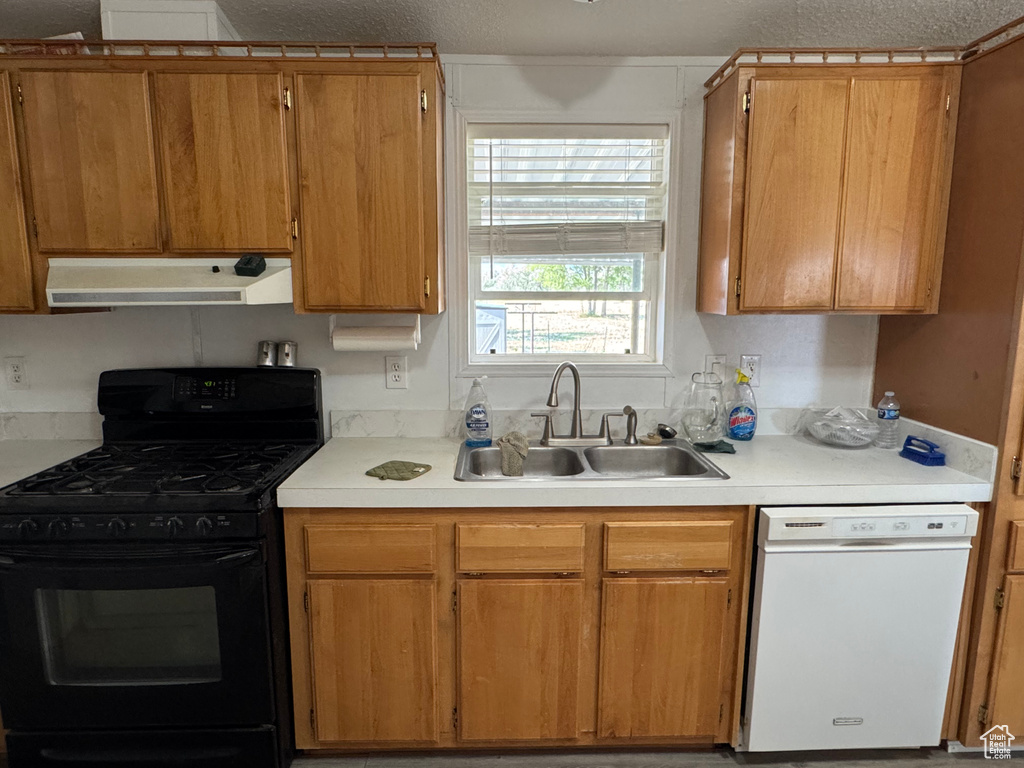 Kitchen featuring black gas stove, dishwasher, under cabinet range hood, a sink, and light countertops