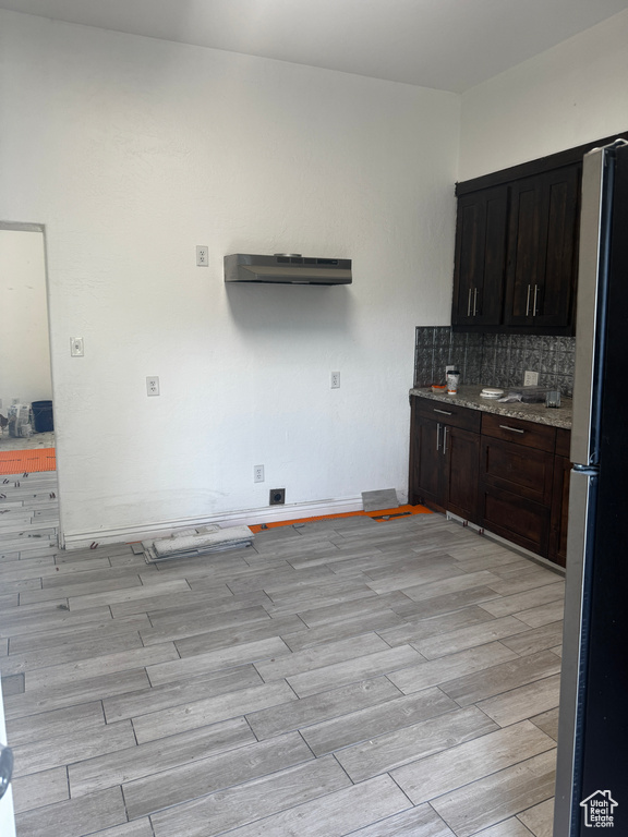 Kitchen featuring freestanding refrigerator, light wood-style floors, decorative backsplash, under cabinet range hood, and dark brown cabinets