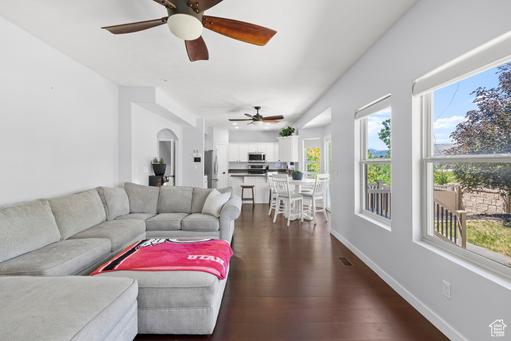 Living room with ceiling fan, dark wood finished floors, baseboards, and arched walkways