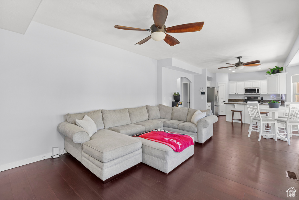 Living room featuring a ceiling fan, arched walkways, dark wood-style flooring, and baseboards